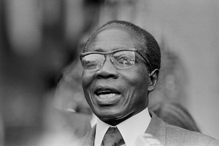 A bespectacled man wearing a jacket, shirt and tie smiles heartily