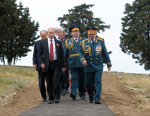 Vladimir Putin walks in the country with a grou pf military officers and intelligence staff.