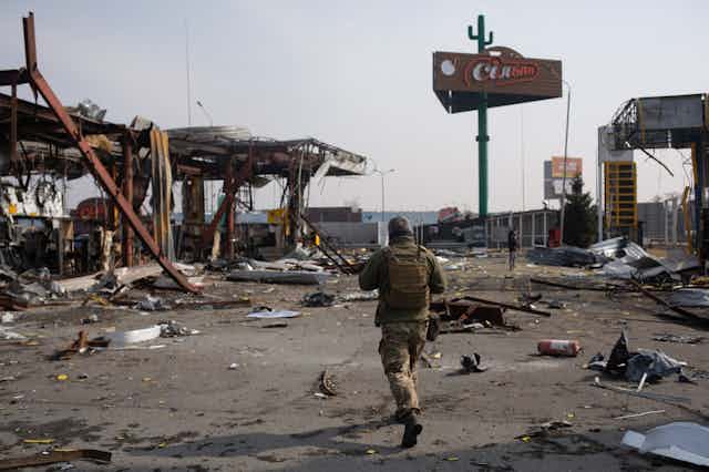 A soldier walks through the rubble of a destroyed gas station.