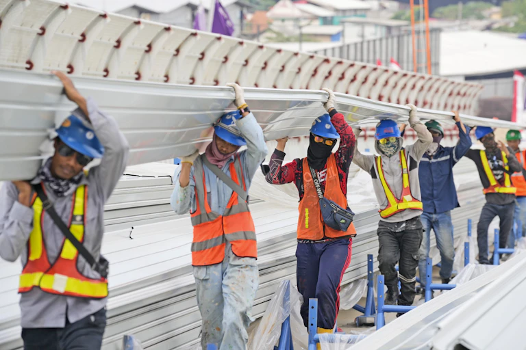 Construction workers carry building material on their shoulders