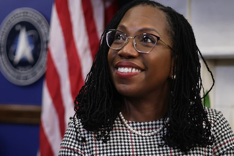 A black woman is smiling with the red aand white stripes of the American flag in the background.d