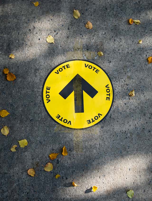 A yellow vote sticker on pavement surrounding by autumn leaves.