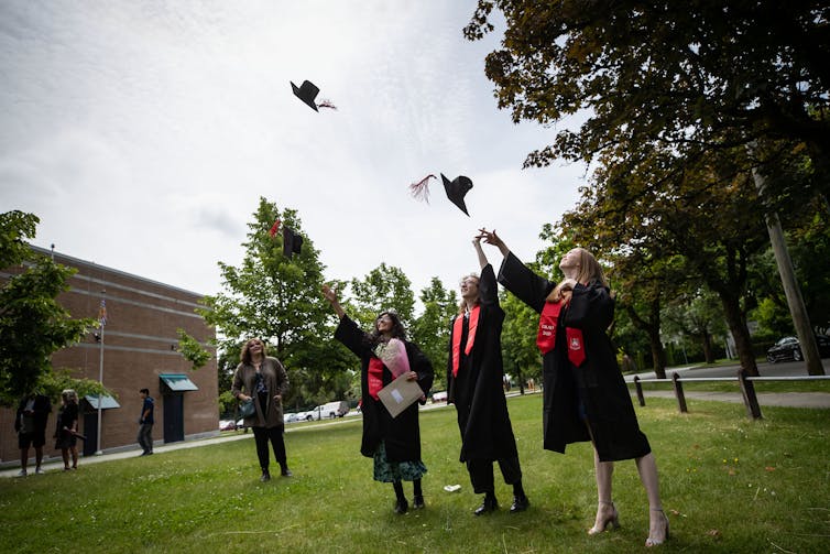 Students toss their graduation caps into the air while posing for family photos.