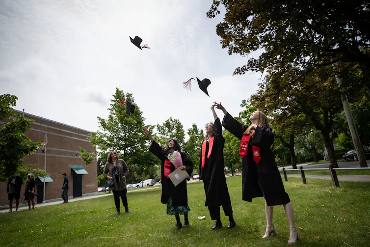 Students toss their graduation caps into the air while posing for family photos.
