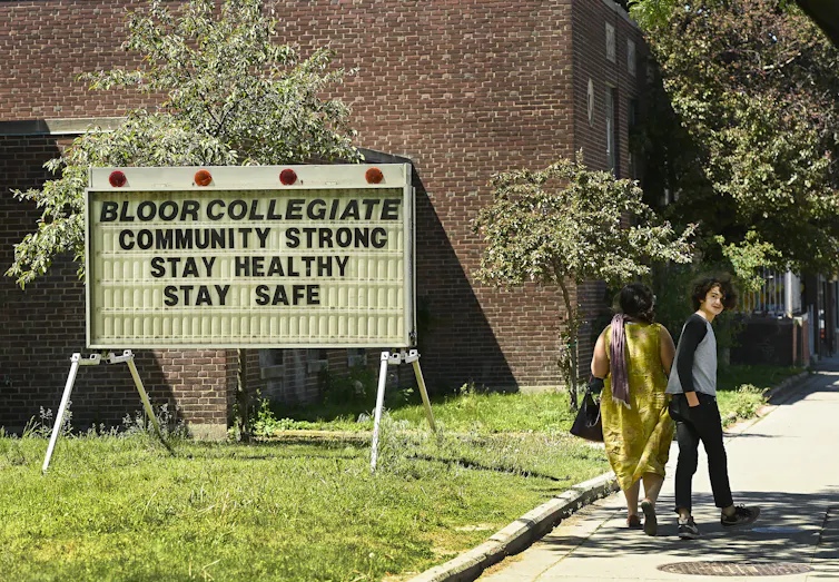 A teenager with a mop of dark hair looks back as he walks past a high school with a friend.