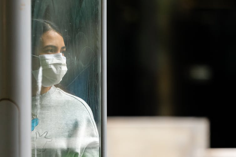 Woman in mask looks out of the window.