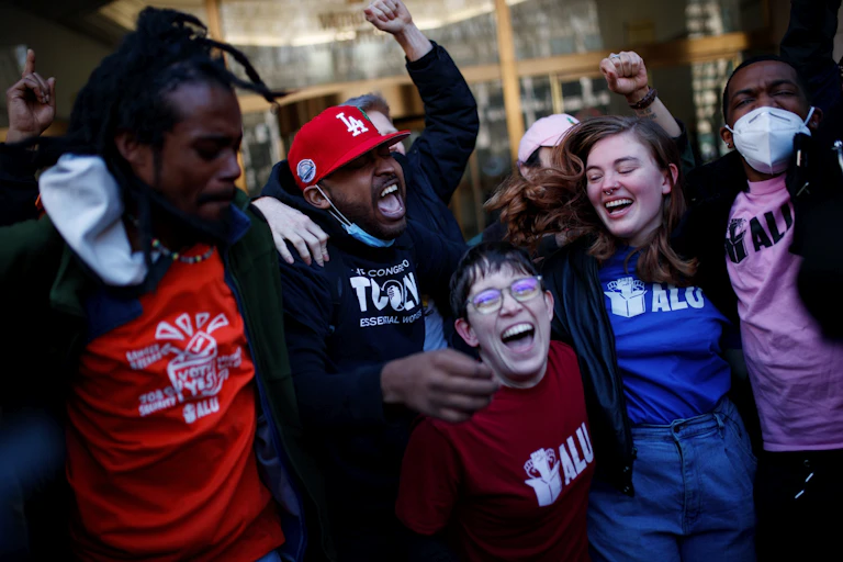 Amazon union members in pro-union t-shirts celebrate and jump in the air.