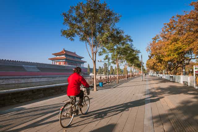 A cyclist wearing red pedals down a path lined with trees in China.