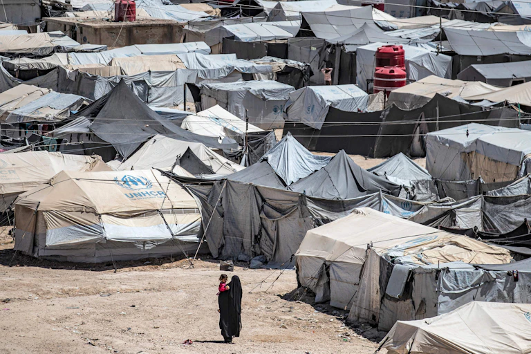 A fully veiled woman carries a child through a refugee camp