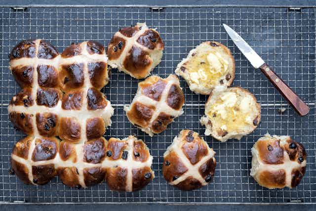 Hot cross buns some cut in half with a butter knife beside them.