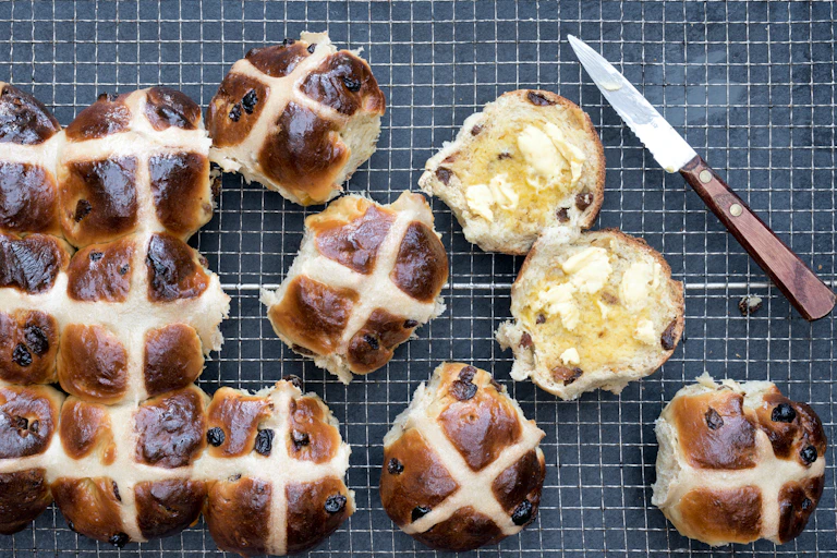 Hot cross buns some cut in half with a butter knife beside them.