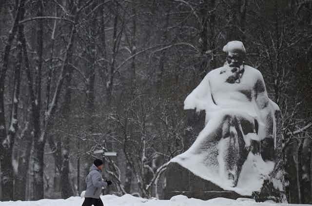 Man jogs by a statue covered in snow.