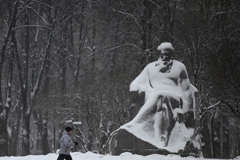Man jogs by a statue covered in snow.