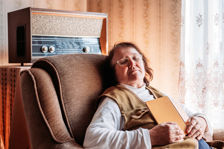 Personne en train de dormir sur un fauteuil, avec un livre dans les mains.