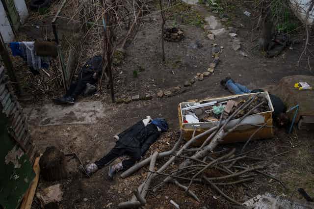 Bodies of several dead people lie on the dirt amid broken tree limbs and rubble.