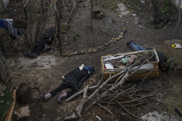 Bodies of several dead people lie on the dirt amid broken tree limbs and rubble.