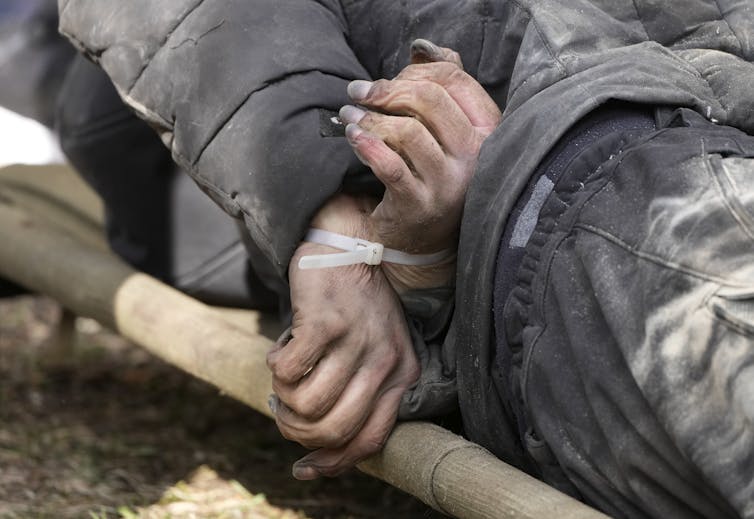 The wrists of a dead person are shown tied together with a zip tie.