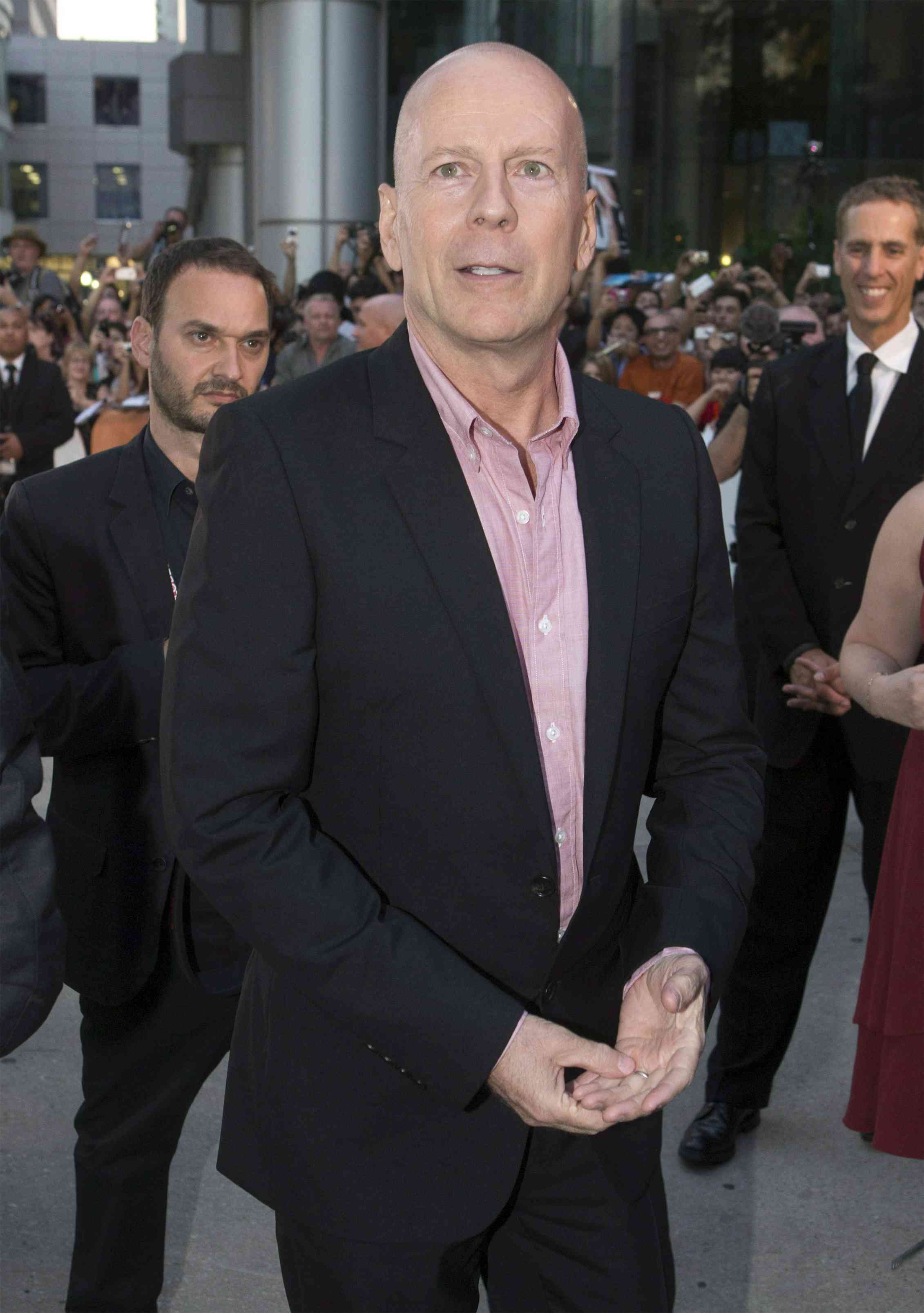 A bald man in a black suit with other people behind him