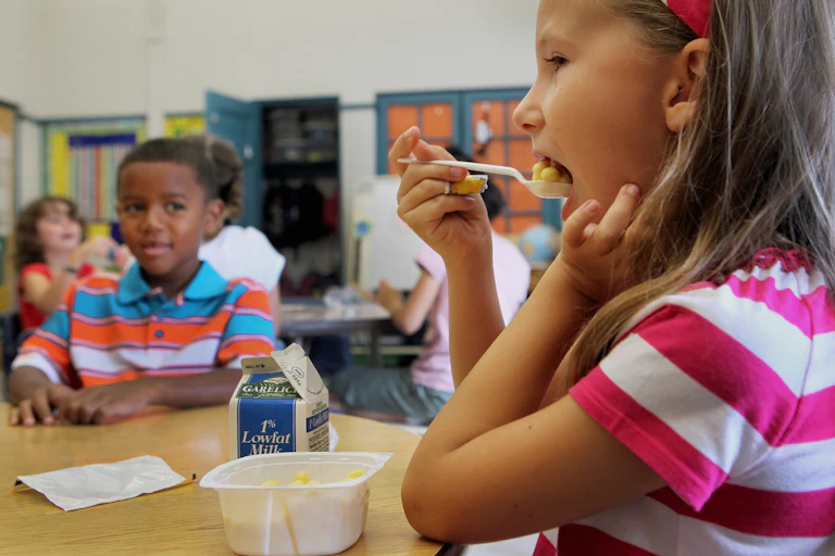 A schoolgirl eats a bowl of cereal in class.