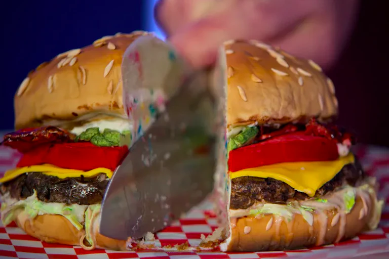Knife cuts through center of a cake made to look like a cheeseburger.