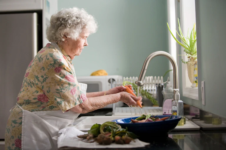 older woman at sink washing vegetables