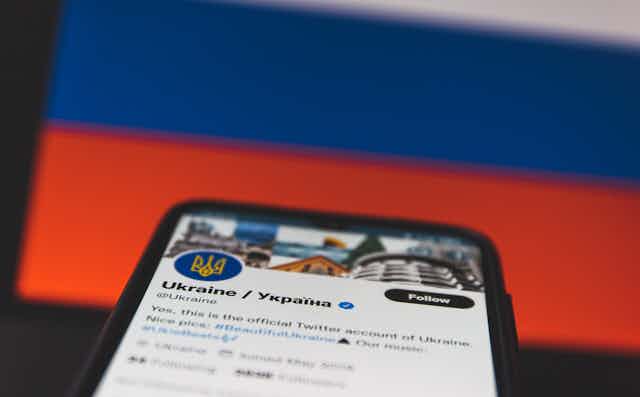 Mobile with Ukraine's Twitter account opened up held is in front  of the Ukrainian flag