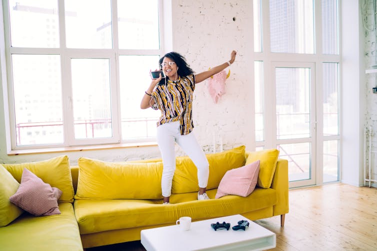 A woman jumps on the couch while singing.