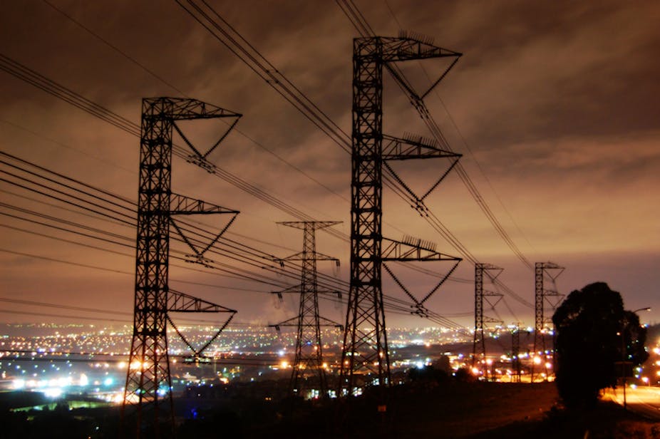 Electricity pylons with a background of city lights and dramatic sky.