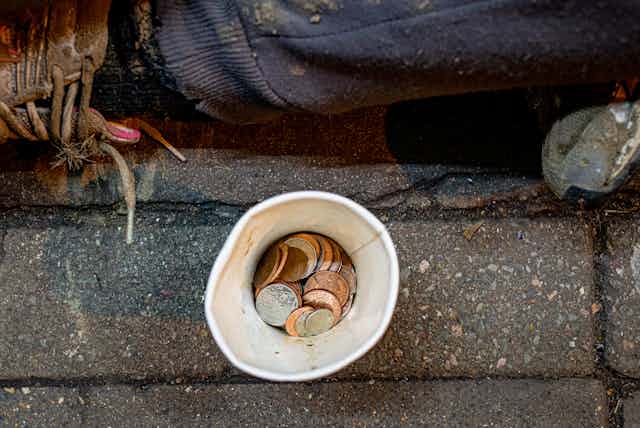 Photo from above of some change in a paper cup in front of a person sitting on the sidewalk