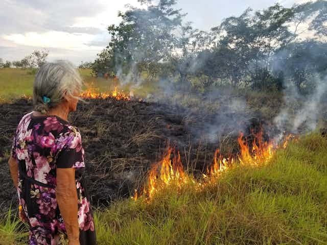 A woman observes a small grass fire.