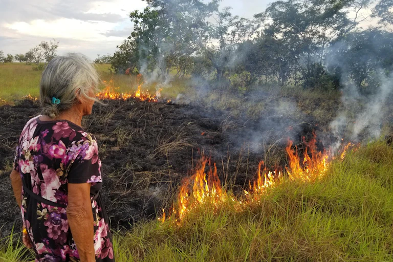 A woman observes a small grass fire.
