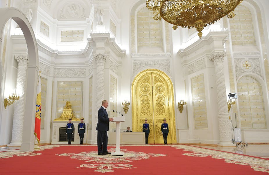 Vladimir Putin making a speech in the Kremlin, flanked by guards and a gold door