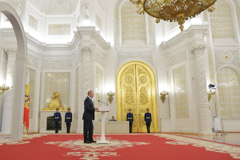 Vladimir Putin making a speech in the Kremlin, flanked by guards and a gold door