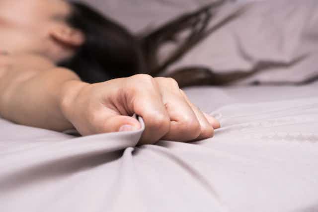 A woman tightly grips a bed sheet