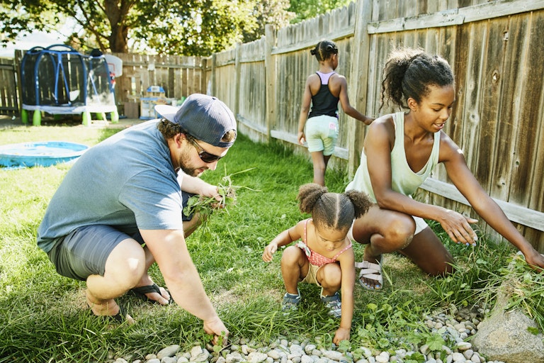 A family with two young children gardens in their yard