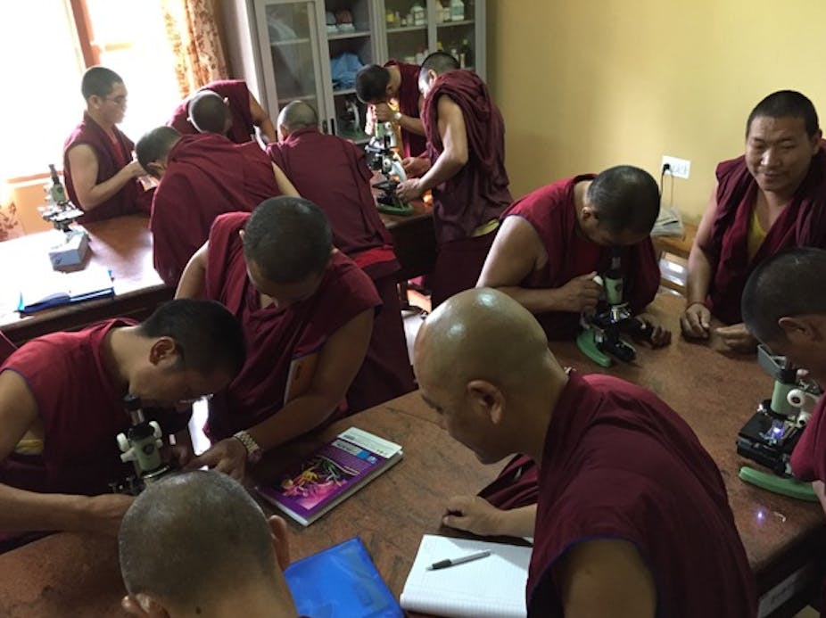 About a dozen monks in red robes work in a classroom.