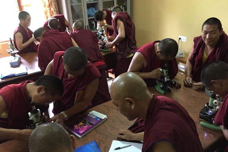 About a dozen monks in red robes work in a classroom.