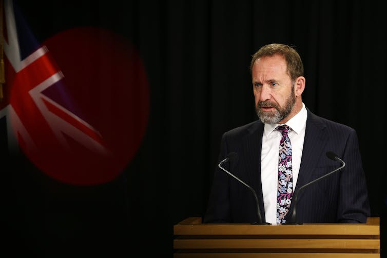 Andrew Little at a podium with a New Zealand flag to his left.
