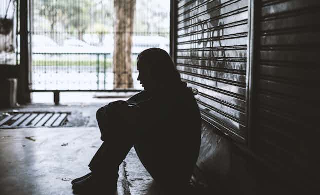 Homeless young woman sits alone on the ground.