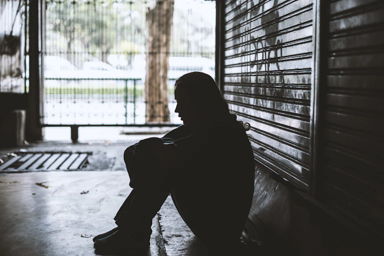 Homeless young woman sits alone on the ground.