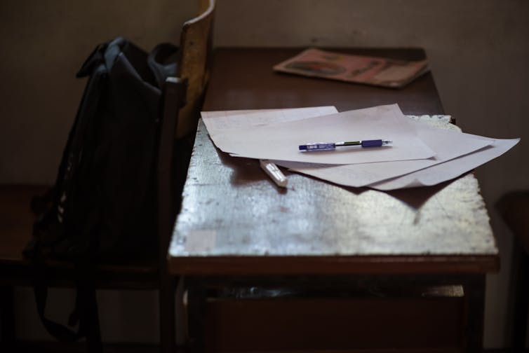 Sheaf of papers and pens on a desk in a dark room.