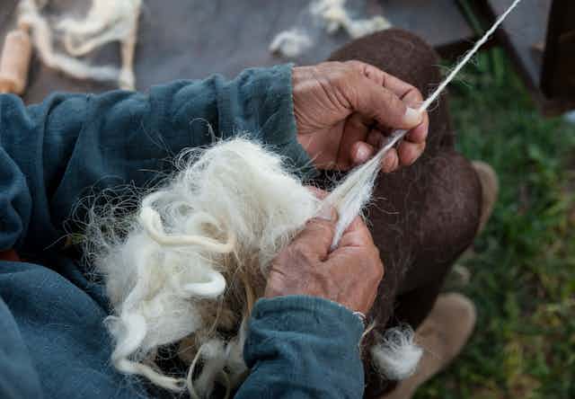 A pair of elderly hands spin a clump of wool into yarn.