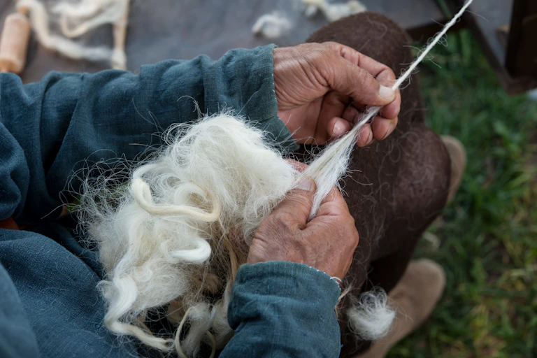 A pair of elderly hands spin a clump of wool into yarn.