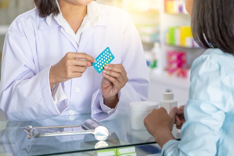 Cropped image of pharmacist's hands holding birth control pills with woman seen from behind