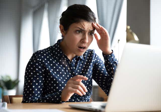 A young woman looks in shock and fear at a laptop screen