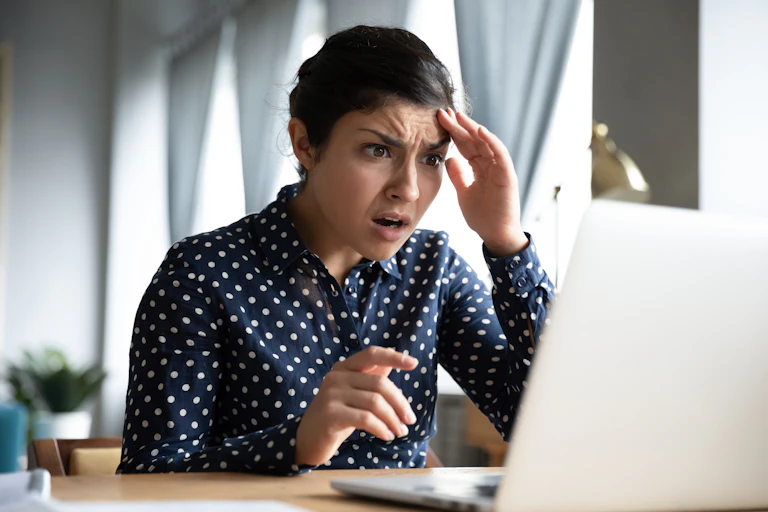 A young woman looks in shock and fear at a laptop screen