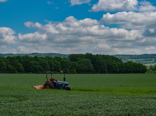 A person drives a tractor across a green field