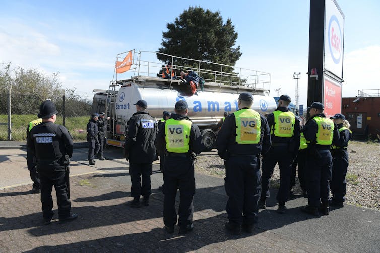 Activists sit atop a silver tanker with police surrounding it.