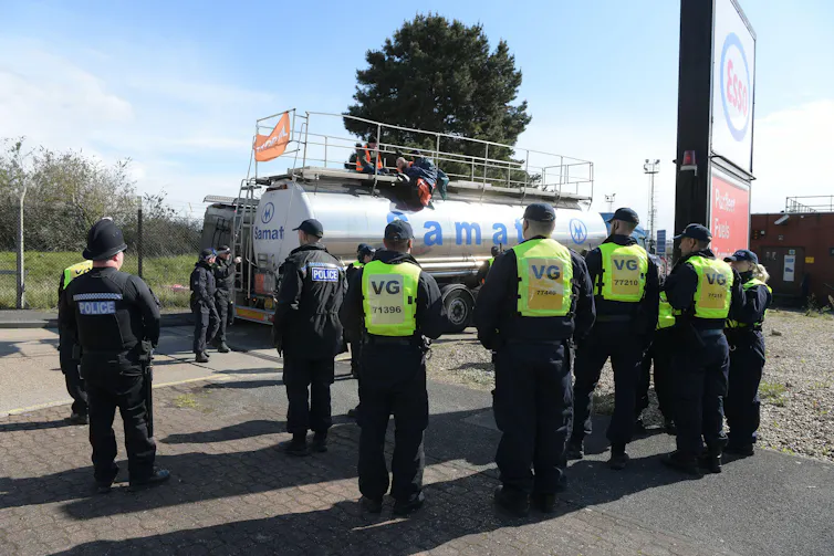 Activists sit atop a silver tanker with police surrounding it.