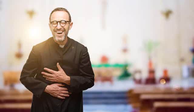 A man in a Catholic priest robe laughs in a church